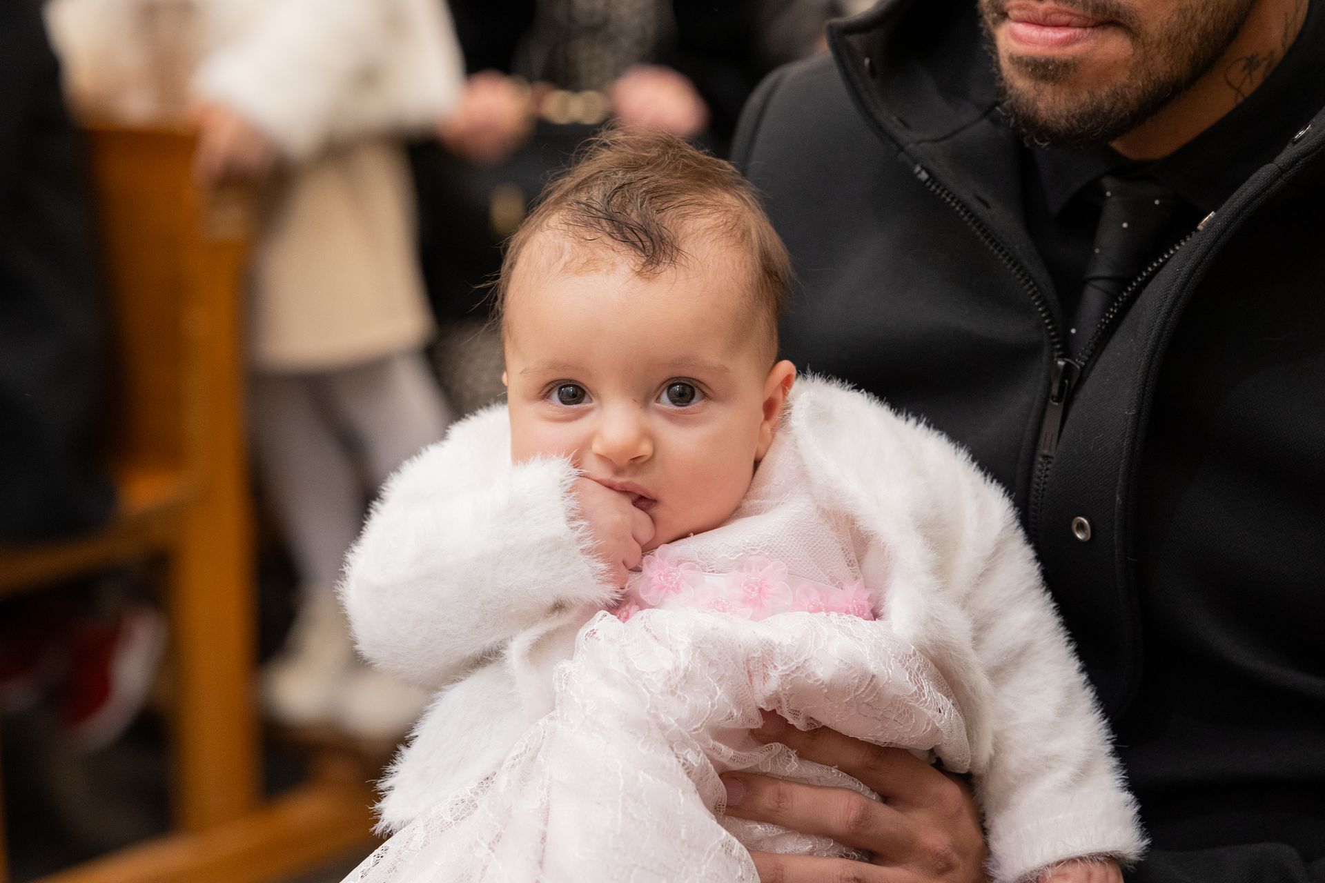 La bambina avvolta in una pelliccia bianca in braccio al papà, fra i banchi della chiesa