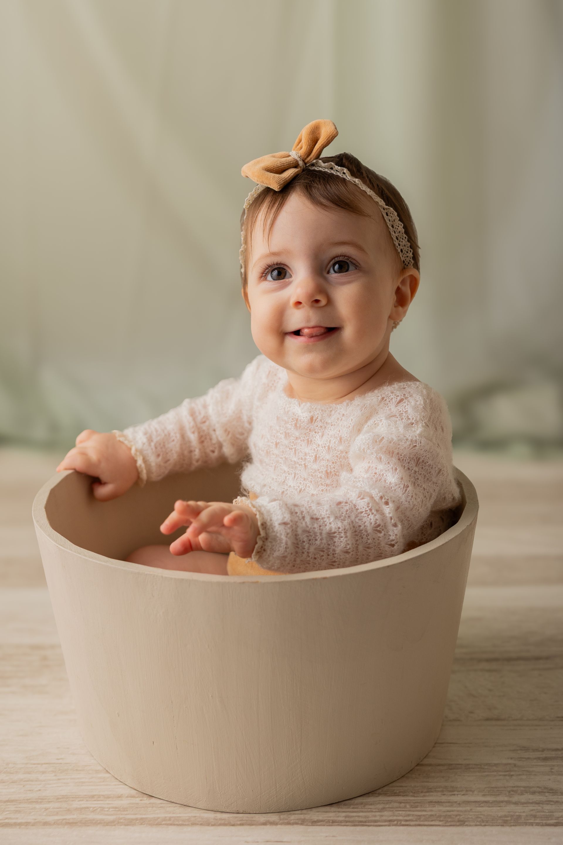 Con un fiocco senape tra i capelli, la bambina sorride affacciata al bordo di un mastello