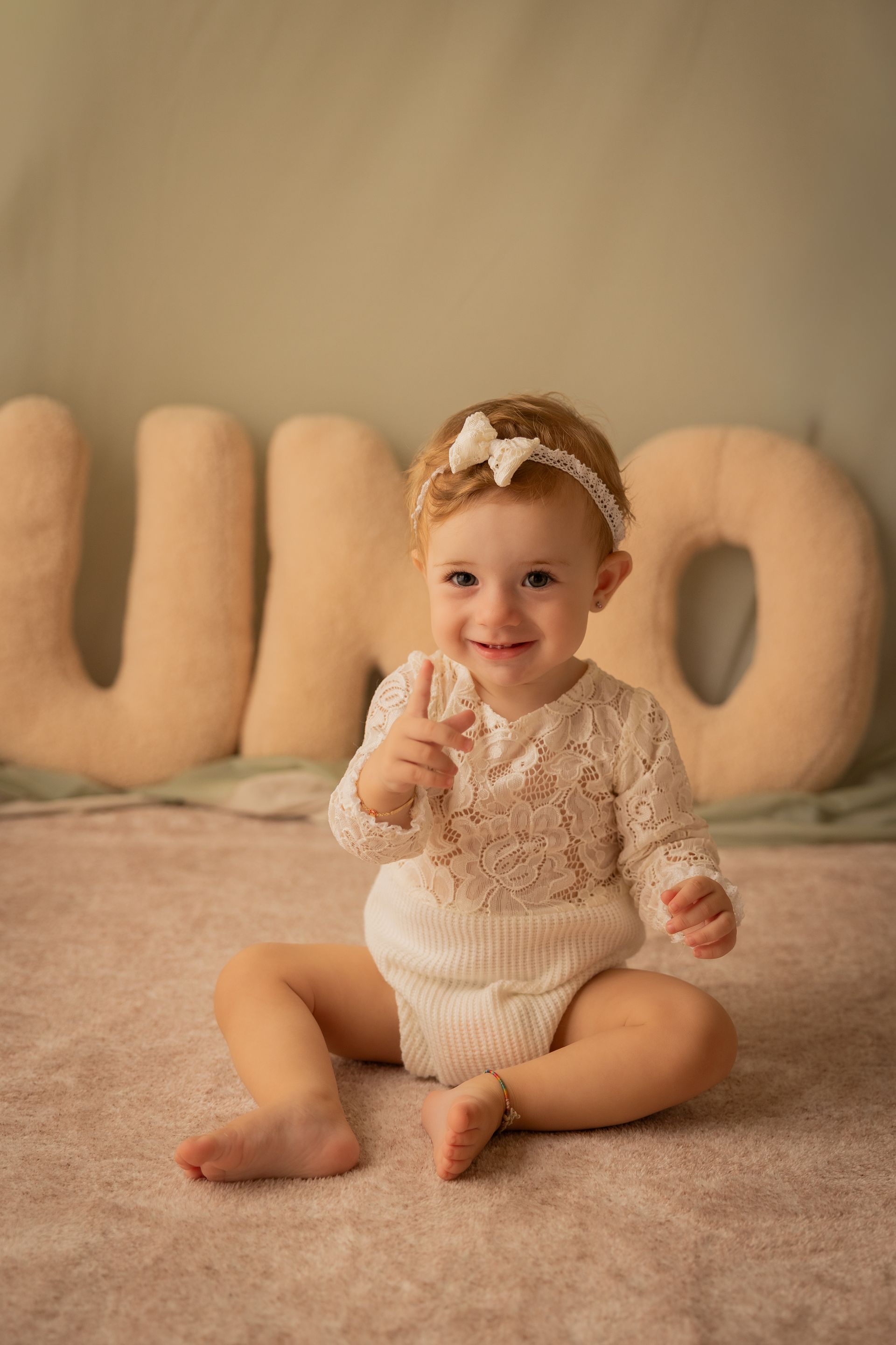 Bambina con fascetta e completo di pizzo bianco seduta davanti a grandi lettere UNO imbottite