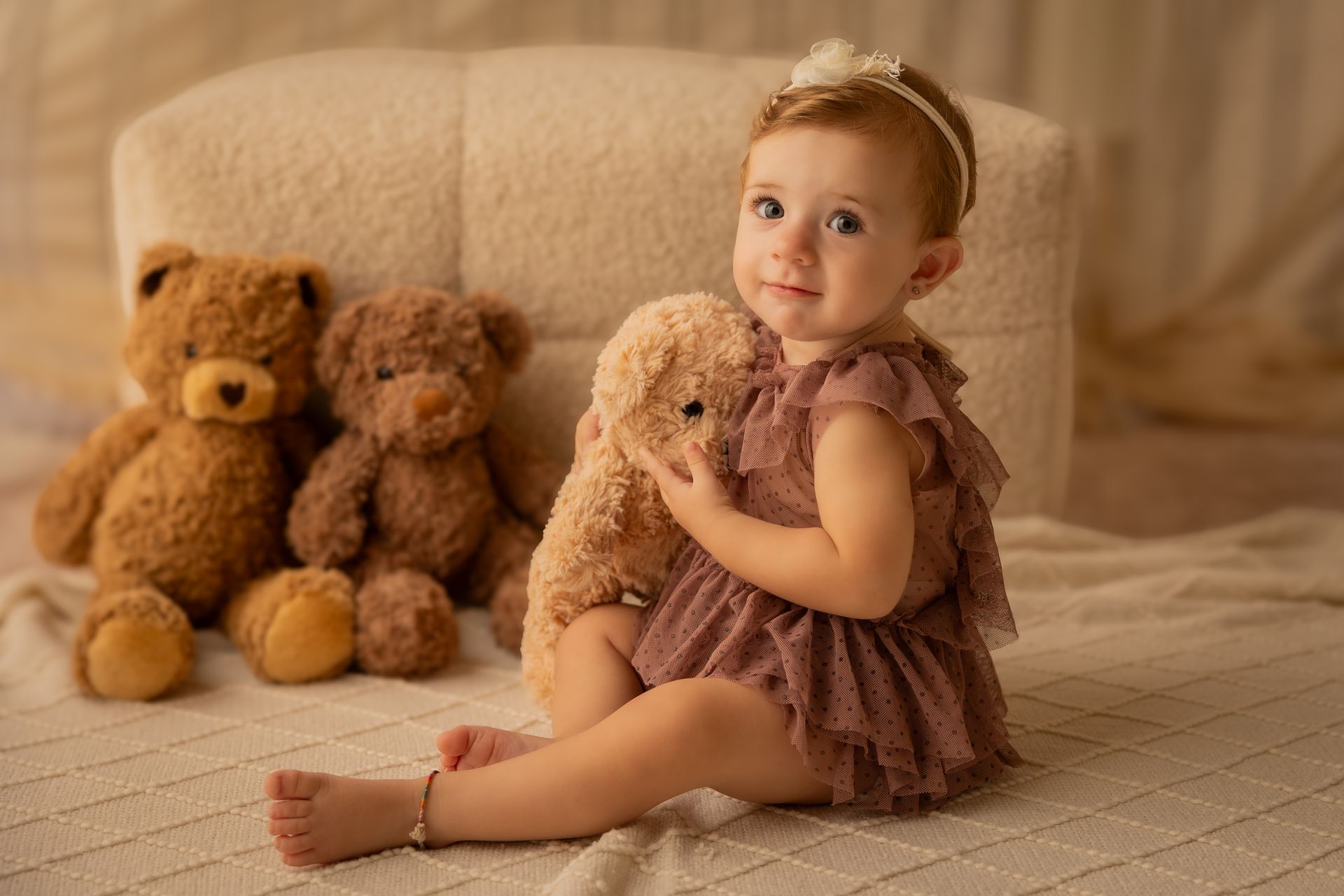Bambina in tulle rosa antico abbraccia un orsacchiotto accanto ad altri peluche su tappeto beige
