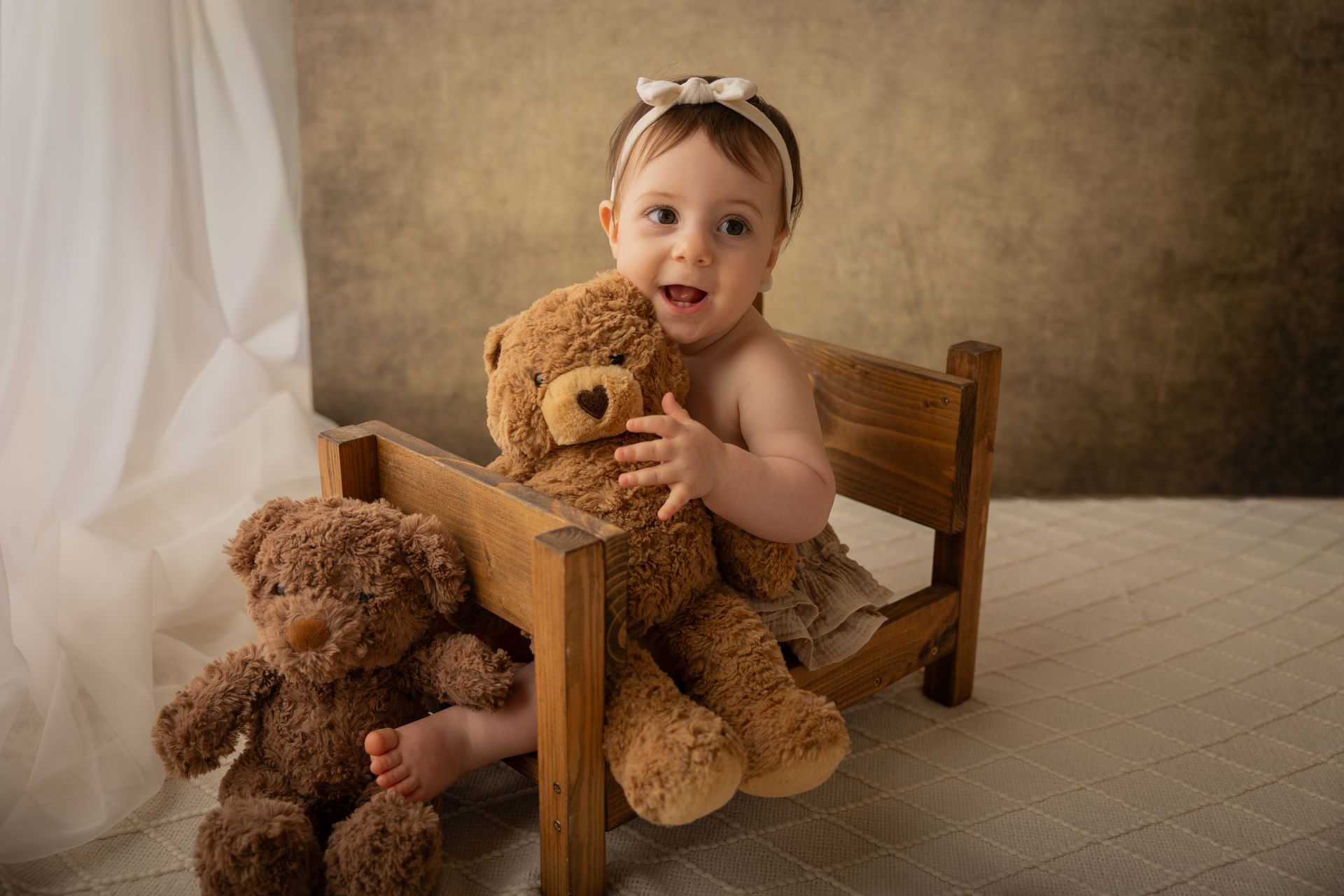 Affacciata da un lettino di legno, la bambina stringe un orsetto mentre altri due riposano sotto