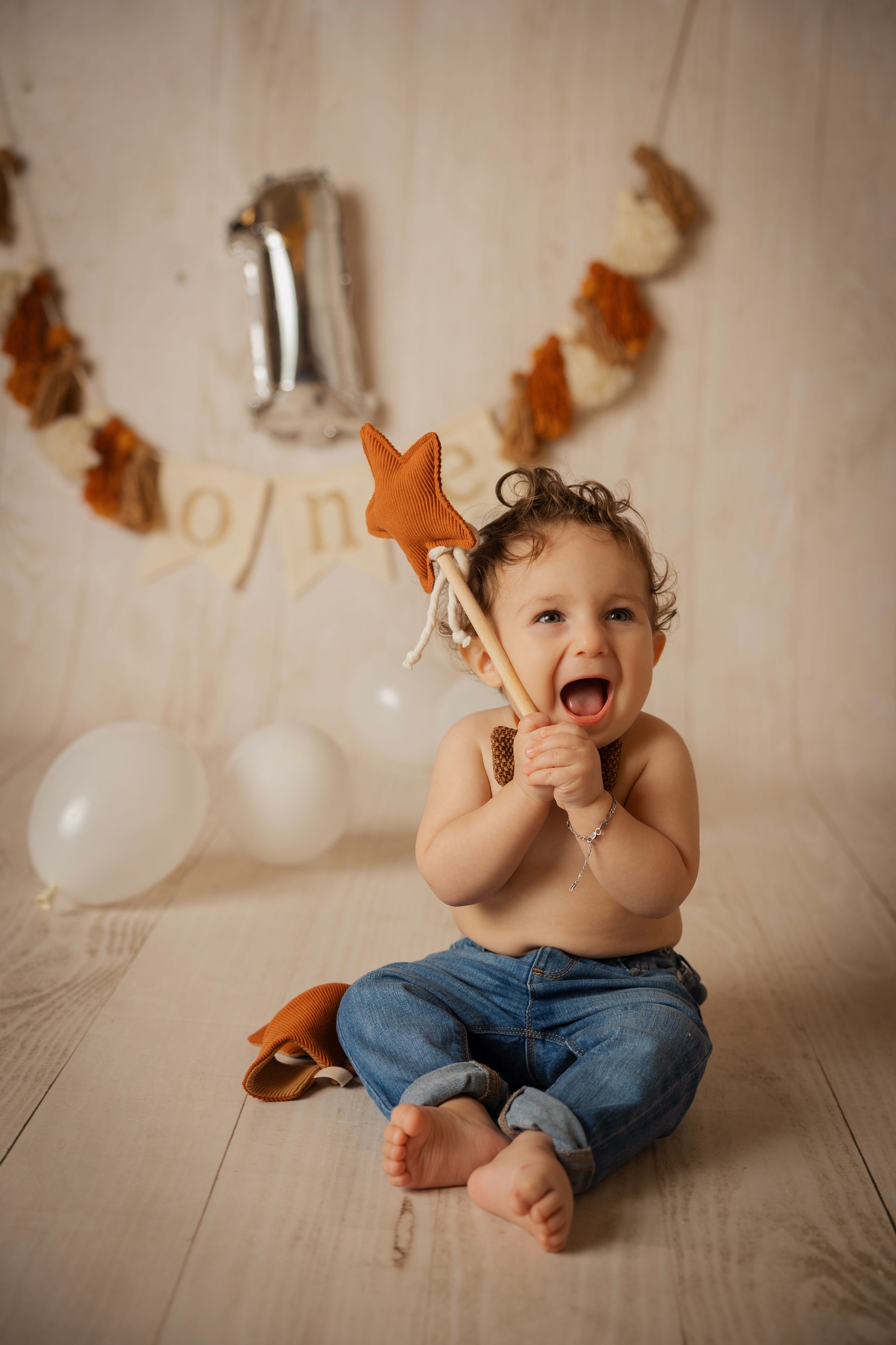 Bimbo a bocca aperta con biscotto a stella, jeans, palloncino argentato numero uno alle spalle