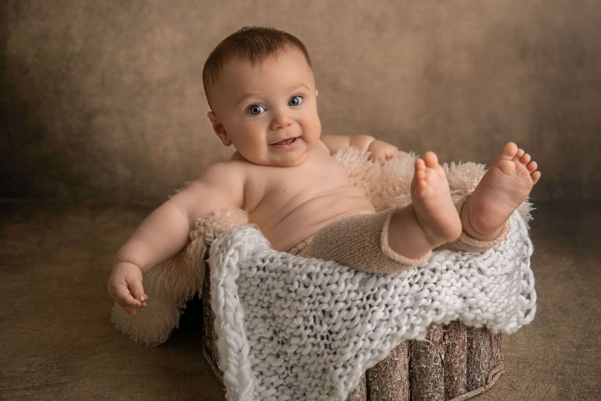 Bambino sorridente seduto in un cesto foderato di pelliccia e lana panna, sfondo marrone caldo