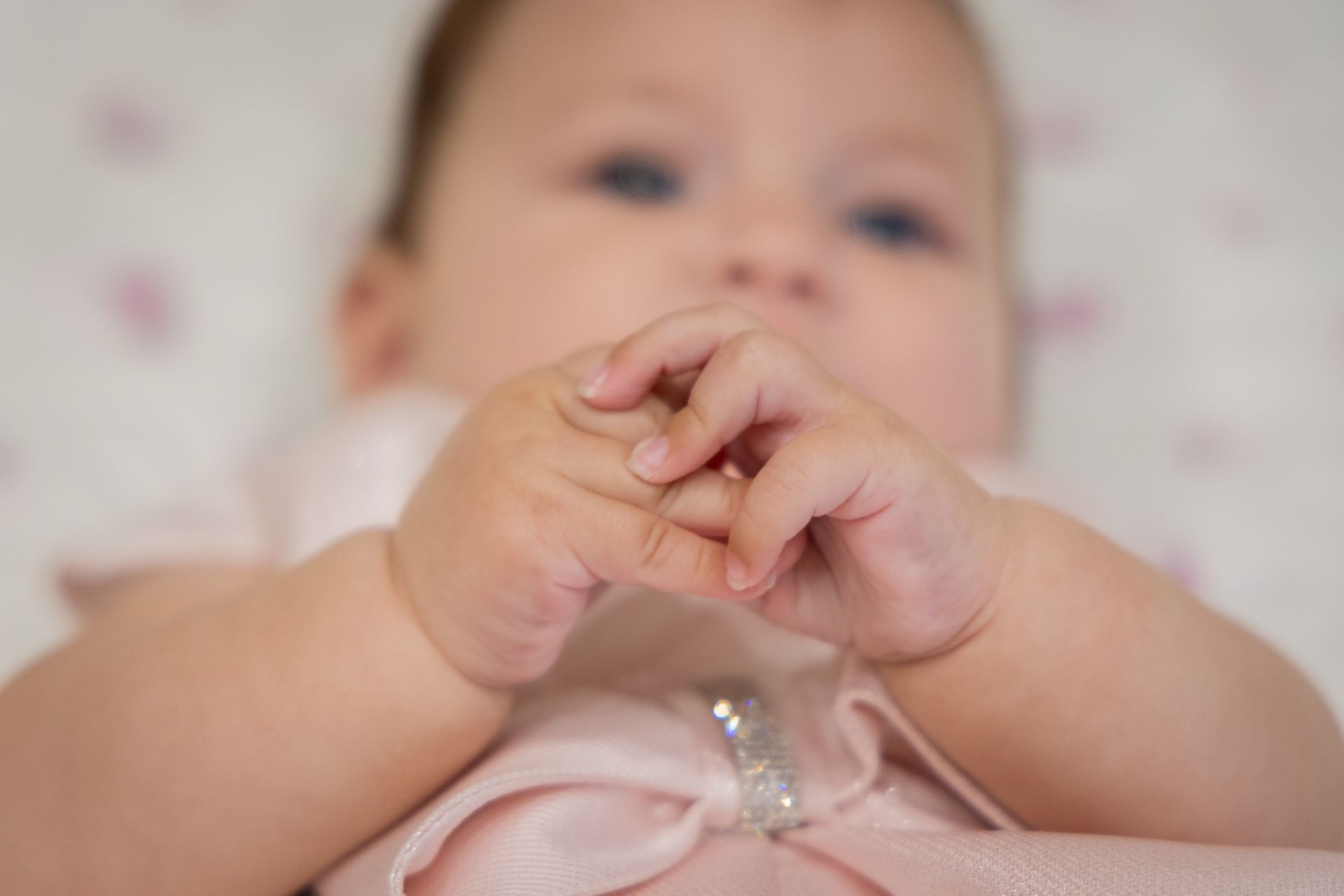 Le mani della neonata che si toccano sopra il body rosa, su un fondo rosa a cuoricini