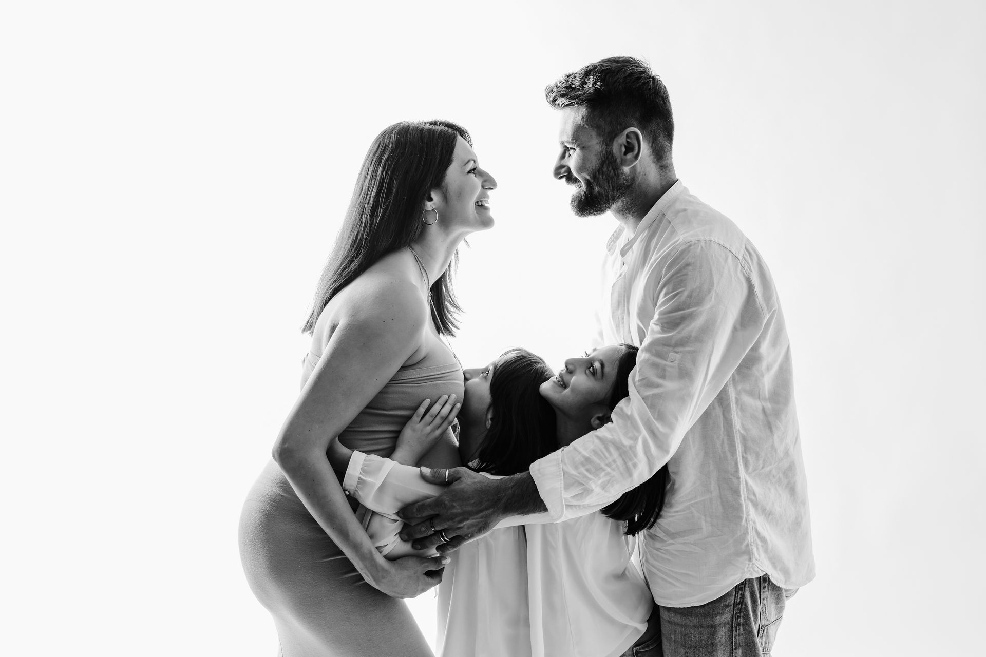Coppia che si sorride con la figlia stretta tra loro, ventre scoperto su fondo bianco, scatto monocromatico