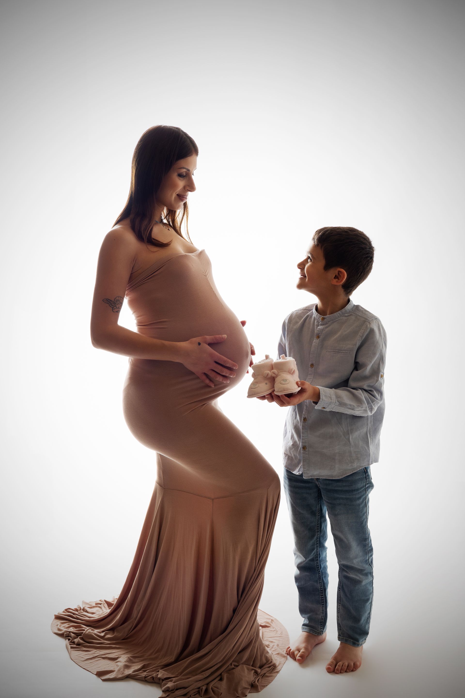 La futura mamma in abito color cipria guarda il figlio più grande che le mostra un paio di scarpine