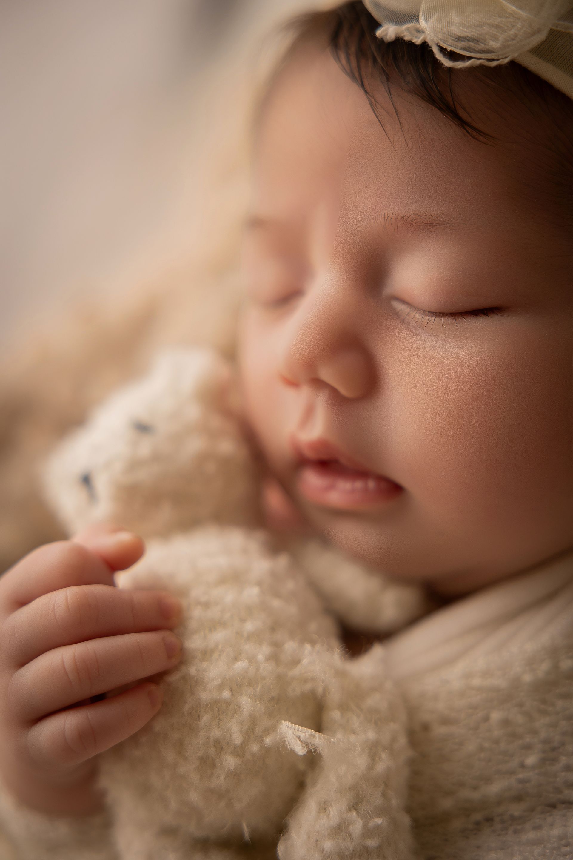 Volto sereno di una neonata addormentata che stringe fra le dita un orsetto di peluche chiaro