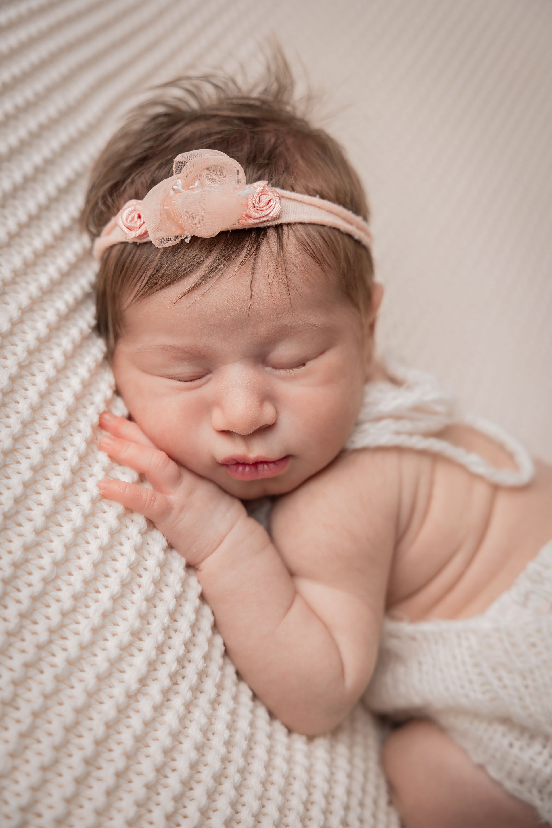 Neonata con una fascia rosa dorme sul fianco con le mani sotto la guancia, su una coperta panna a coste