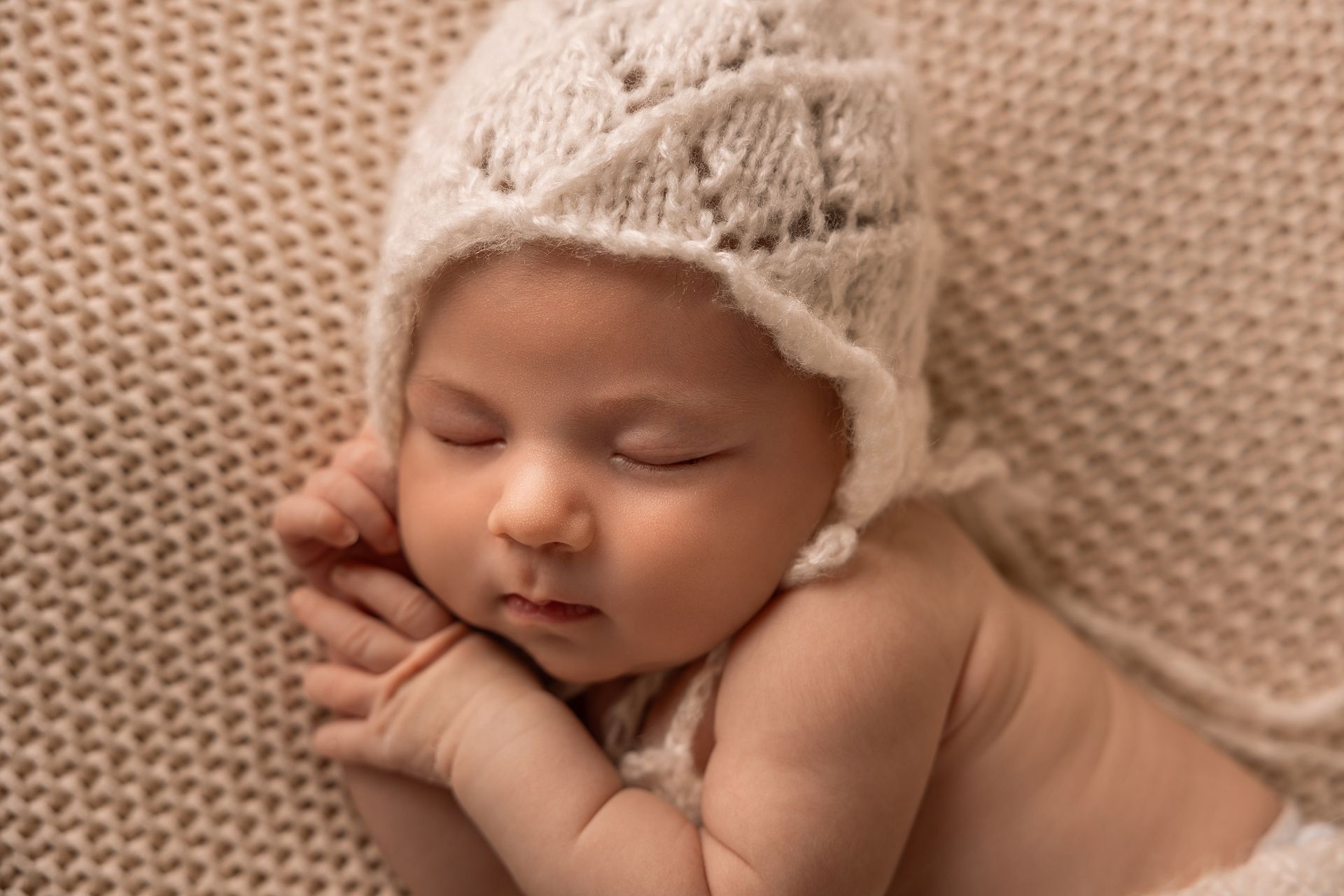 Neonata con cuffietta di lana rosa dorme con le manine raccolte sotto la guancia