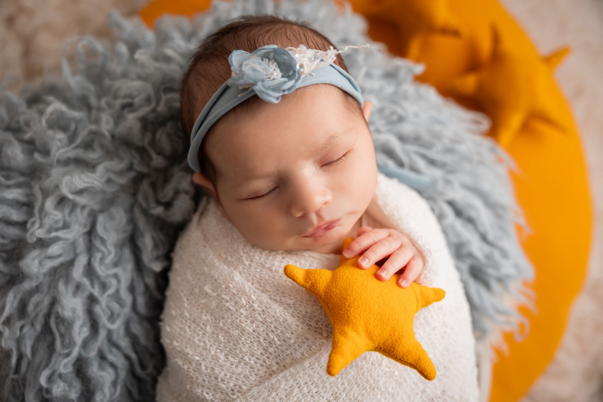 Neonata con fascia azzurra dorme avvolta nel bianco su pelliccia grigia dentro un cesto giallo