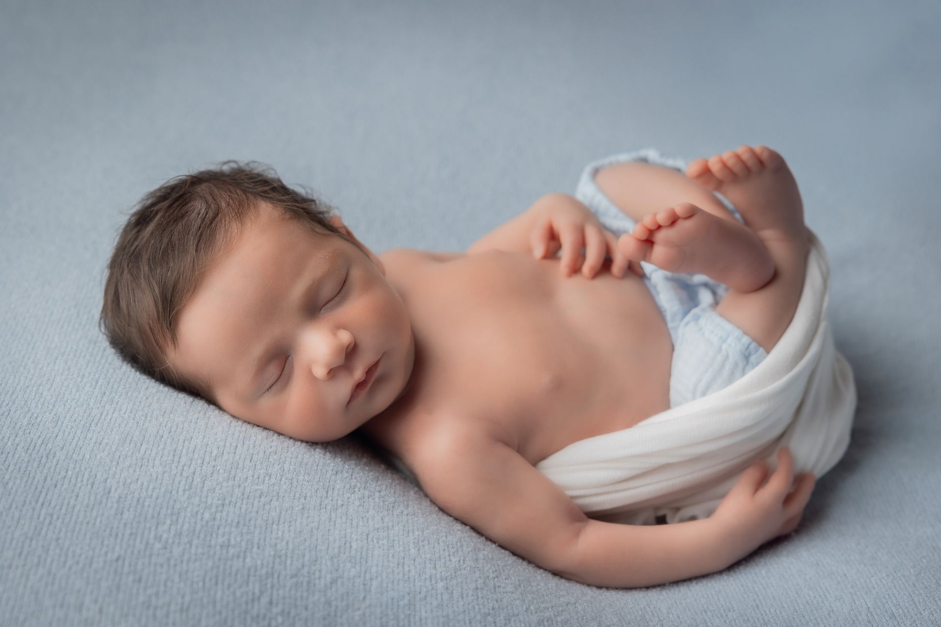 Neonato che dorme su un fondo azzurro, avvolto in parte da un telo bianco