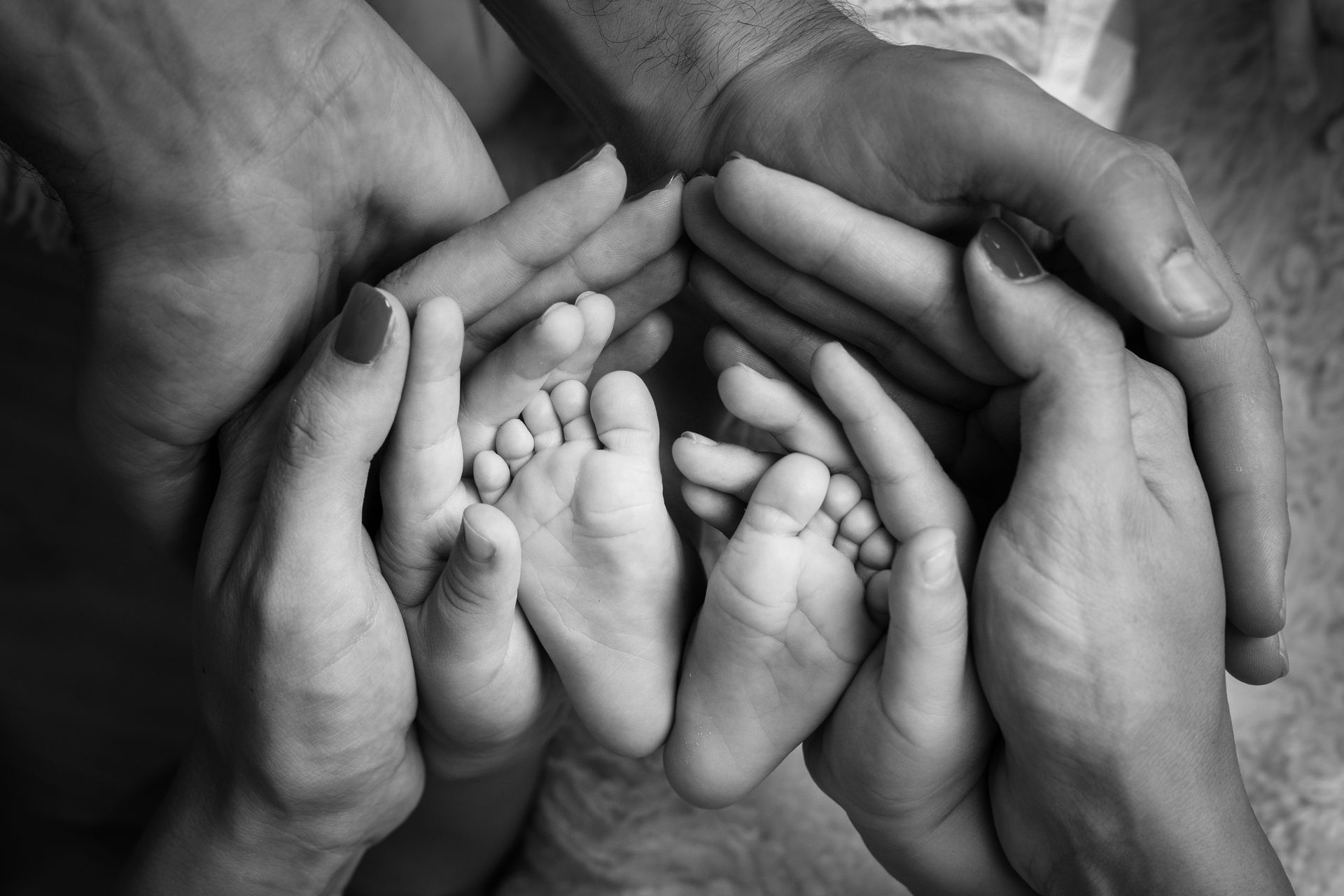 Piedini di un neonato raccolti nelle mani sovrapposte dei genitori, ripresi da vicino in bianco e nero